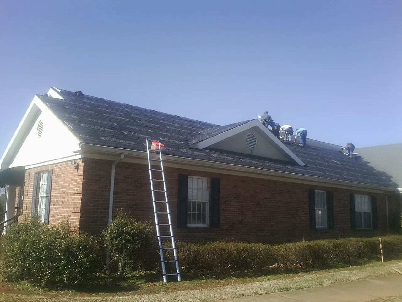 Crew tearing shingles off a brick ranch roof with a ladder set — Emergency Roof Repair work by our crew in Gilroy