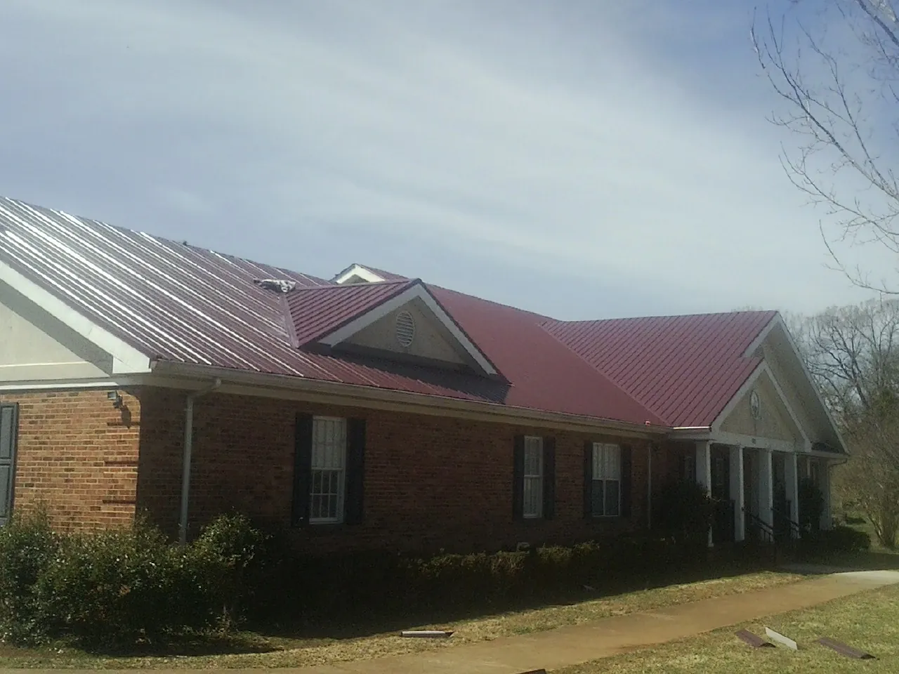 Red metal roof with gabled entries on a long brick building, from a Hail Damage Roof Repair job in Gilroy