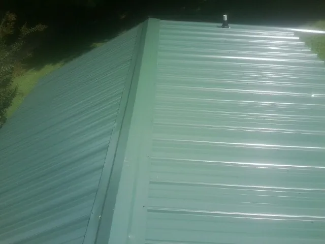 New green metal panels meeting at the ridge of a roof — Flat Roof Repair work by our crew in Gilroy
