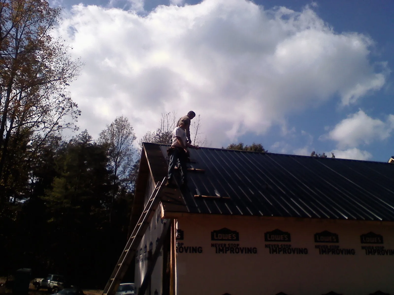 Roofer fastening dark metal panels high against a cloudy sky, from a Roof Inspection job in Gilroy