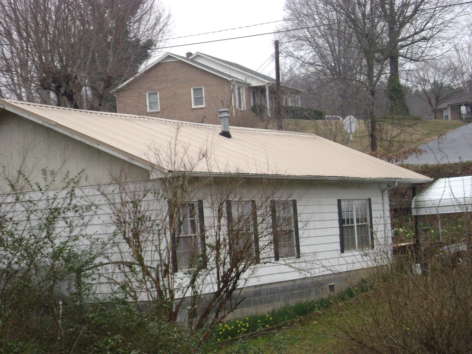 Tan metal roof on a white sided house set into a hillside — Commercial Roofing by Roofing Brothers in Gilroy